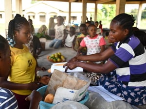Una mujer en un mercado en República del Congo le entrega a su clienta una hogaza de pan envuelta en papel