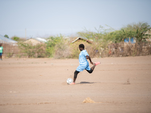 Una niña se prepara para patear un balón en un campo cubierto de polvo.