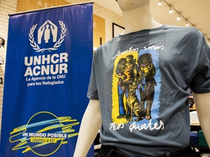 Un banner con el logo de ACNUR junto a un maniquí que lleva una camiseta con una ilustración impresa