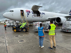 Una mujer y un hombre con chalecos azul y amarillo, respectivamente, de espaldas frente a un avión de cargo de LATAM.
