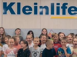 Un grupo de niñas y niños refugiados debajo de un letrero que dice Kleinlife