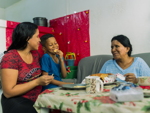 Una mujer, su madre y su hijo sonríen mientras comen tras la jornada laboral dela joven