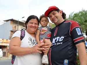 Una familia compuesta por un hombre, una mujer y el bebé que cargan en sus brazos, sonríe posando para la foto.