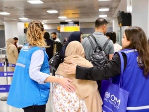 Dos mujeres que llevan puestos chalecos azules acompañan a una mujer que lleva un velo en su cabeza en un aeropuerto.