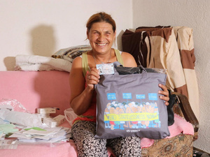 Una mujer sentada en una cama sostiene un bolsa gris y un documento de identidad