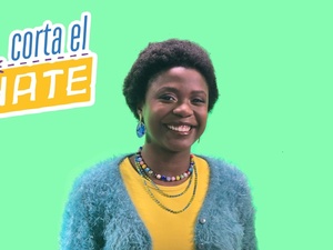 Una mujer que viste suéter azul y playera amarilla sonríe frente a un fondo verde