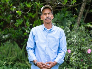 Un hombre de camisa azul y gorra frente a un jardín