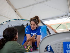 Una mujer con camisa de ACNUR habla con otra mujer en un campamento transitorio.