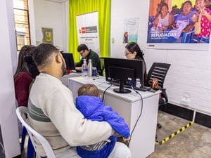 De espaldas, un hombre sentado en una silla frente a un escritorio, sostiene a un bebé que viste chamarra azul