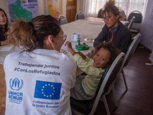 Sentados a la mesa con alimentos se encuentran dos mujeres, una joven y un niño sonriente