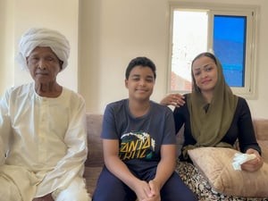 Un niño sentado en un sofá entre su abuelo y su madre en su apartamento.