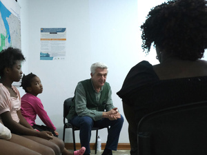 Colombia. Visita del Alto Comisionado, Filippo Grandi, a la región del Darién. Al fondo un hombre sentado en una silla, charla con tres personas que están sentadas de espaldas y de perfil.