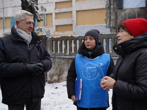En un paisaje urbano nevado, un hombre muy abrigado charla con dos mujeres.