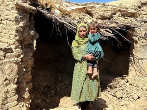 Una mujer afgana sostiene en brazos a su hija de dos años frente a su casa, que quedó dañada por las inundaciones que azotaron el pueblo en el que vivía