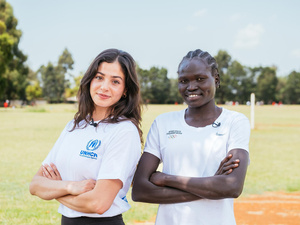 Dos mujeres de brazos cruzados con camisetas blancas de las olimpiadas, posan para la foto en un campo verde