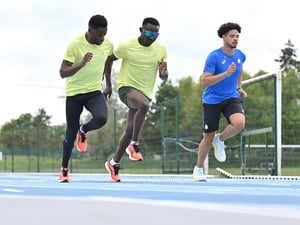 Tres atletas corren en paralelo en una pista azul