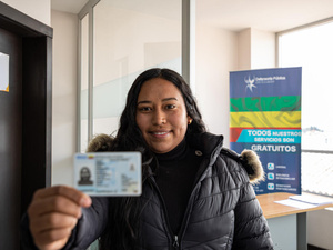 Una mujer muestra sonriendo su cédula. Los datos no son legibles.