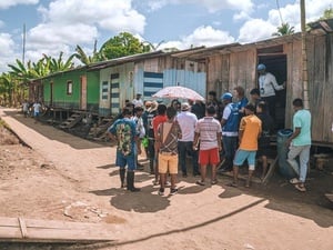 Un grupo de personas reunidas fuera de una casa en un area rural interactuando con funcionarios de ACNUR.