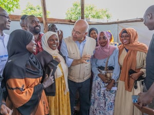 Un grupo de mujeres y hombres, con el Alto Comisionado de las Naciones Unidas para los Refugiados, Barham Salih, en el centro, conversa sonriendo. 