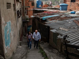 El Alto Comisionado recorre un callejón empinado en medio de casas de ladrillos y techos de zinc acompañado por Andriuska, una joven mujer, que camina a su lado.