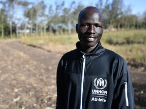En un campo de cultivo, un hombre joven sursudanés sonríe a la cámara
