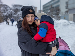 Una mujer ucraniana abraza a su hijo de dos años; ambos llevan puesto ropa de invierno. Detrás suyo, un paisaje urbano lleno de nieve.