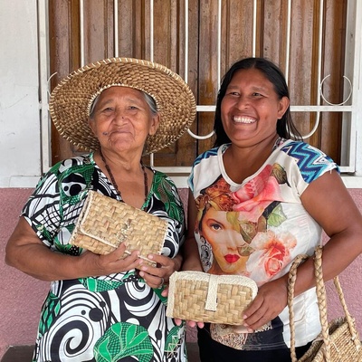 Dos mujeres del pueblo warao, cuyo territorio se encuentra en lo que hoy se conoce como Venezuela, sonríen a la cámara mientras muestran artesanías elaboradas por ellas