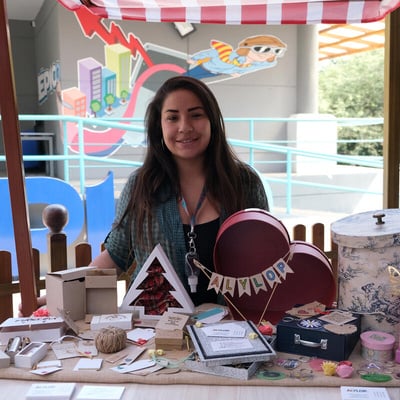 Una mujer refugiada en un puesto en una feria de emprendimientos en donde está promocionando su negocio