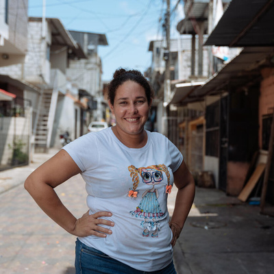 Una mujer de cabello rizado que lleva puesta una camiseta blanca sonríe a la cámara