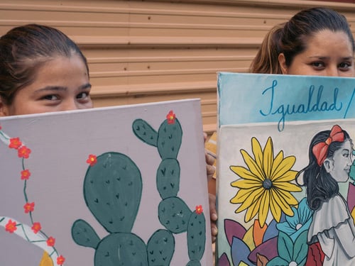 Dos mujeres solicitantes de asilo muestran las pinturas que hicieron