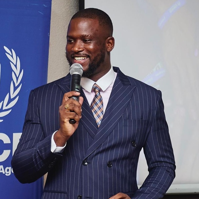 Kwame Annom (Biishville) de saco y corbata hablando con un micrófono en un evento de ACNUR..