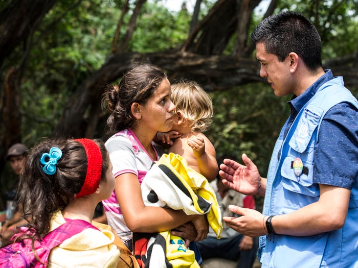 Una mujer con dos niños pequeños charla con un trabajador de ACNUR en Colombia.
