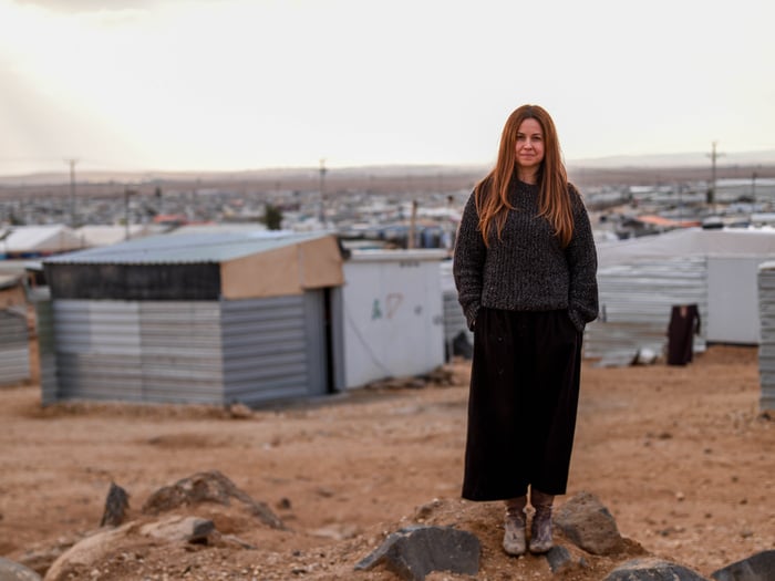 Una mujer que lleva una atuendo negro que llega hasta sus tobillos mira a la cámara en medio de un campamento de refugiados