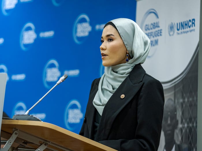 Una mujer afgana que lleva puesto el hijab emite un discurso desde un podio. Detrás suyo, un fondo azul con el logotipo de ACNUR.