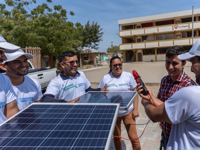 Un grupo de personas sonríen entre sí mientras sostienen juntas un panel solar