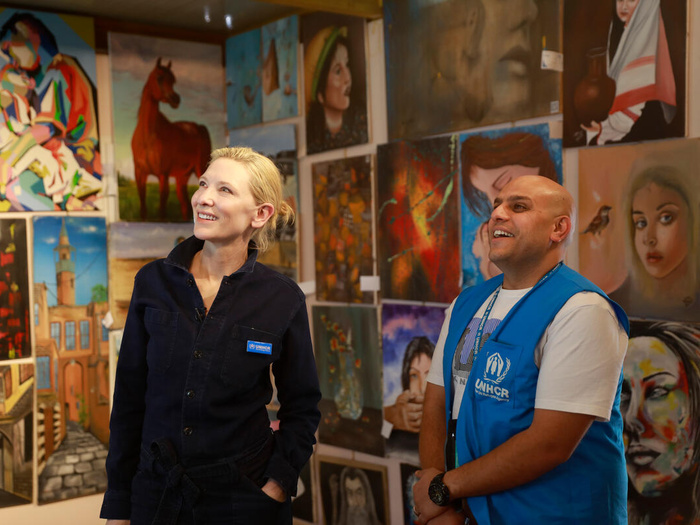 Junto a un trabajador de ACNUR, una mujer rubia admira las obras artísticas que cuelgan de los muros del recinto