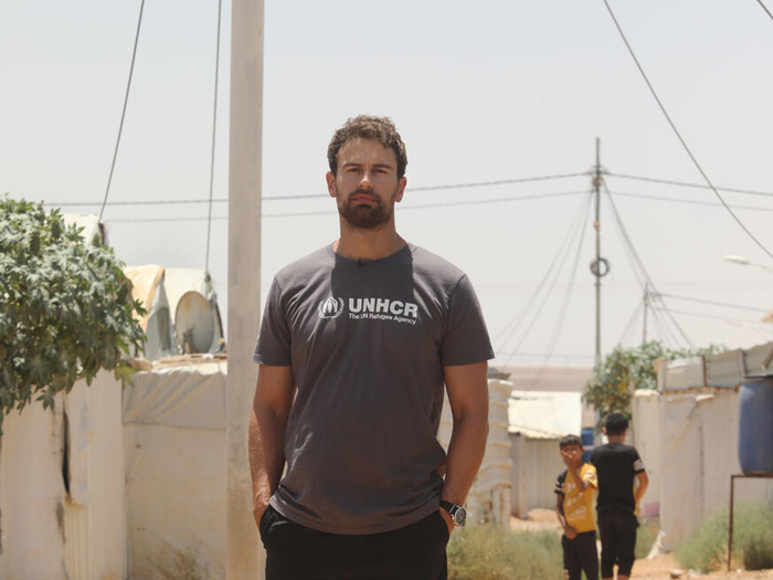En un campamento de refugiados, un hombre con barba que lleva puesta una camiseta con el logotipo de ACNUR mira a la cámara