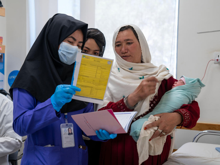 Tres mujeres que llevan puesto un hiyab observan un registro médio. Una de ellas (izquierda) lleva en brazo a un bebé.
