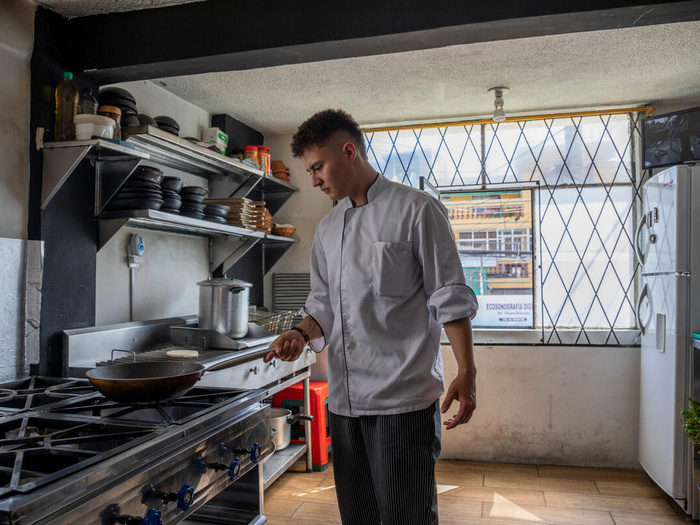 Un joven cocinero frente a una estufa, moviendo una sartén