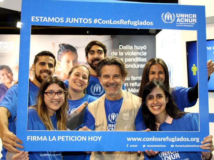 Un grupo de personas con la imagen de ACNUR sostiene un marco de fotos azul que dice "Estamos juntos #ConLosRefugiados" y "Firma la petición hoy"