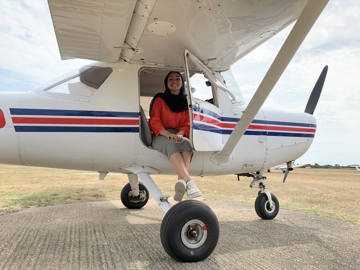 Una joven siria, que lleva puesto un hiyab color negro, sonríe a la cámara montada en una avioneta blanca con rayas rojas y azules en el medio