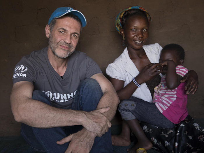 Un hombre con barba, que lleva puesta una gorra, sentado junto a una mujer africana que tiene a una cría suya en su regazo