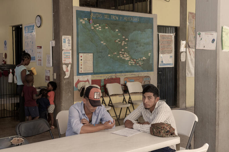 Dos hombres sentados ante una mesa. Detrás hay un mapa de México.