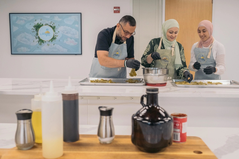 Un hombre y dos mujeres, que llevan puesto el hijab, preparan un platillo tradicional sirio en una cocina