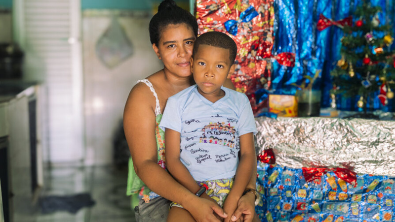 Un mujer joven abraza a su hijo; ambos miran a la cámara