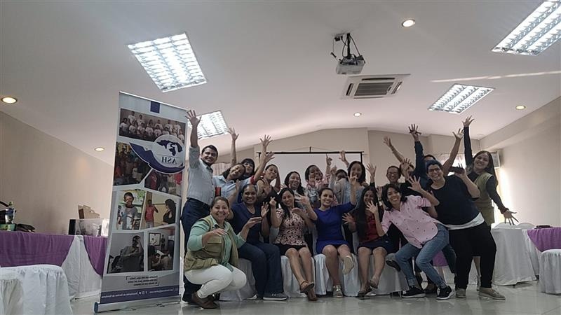 Un grupo de alrededor de veinte personas posan para la cámara en un salón de conferencias en el que hay mesas cubiertas con manteles y un banner con información sobre la Asociación de Sordos de Honduras