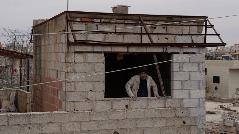Un hombre con sombrero enmarcado en una ventana sin cristales de un edificio de bloques de cemento