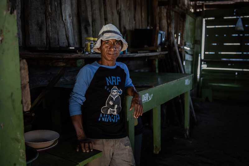 Un hombre con un sombrero de pescador posa frente a cámara en una sencilla casa de madera.
