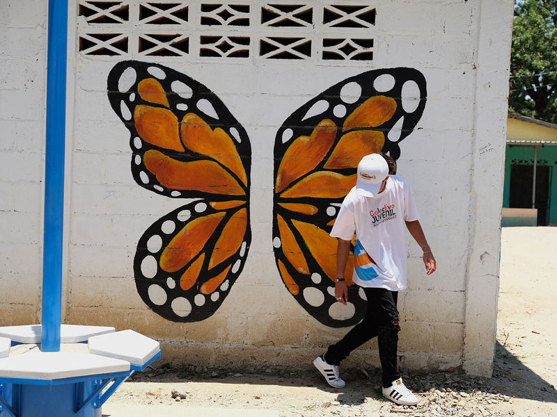 Un joven fotografiado junto a un mural de gran tamaño que representa una mariposa.