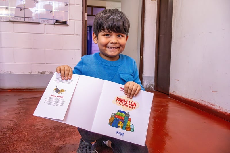 Un niño sonríe para la cámara mostrando un libro ilustrado